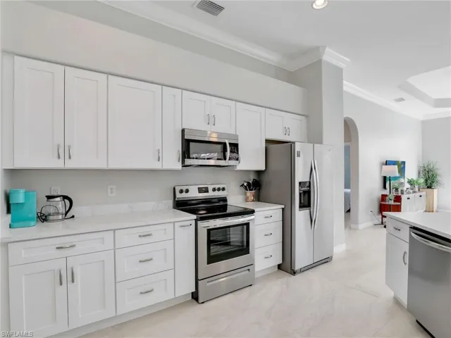 Kitchen featuring stainless steel appliances, ornamental molding, arched walkways, and white cabinetry