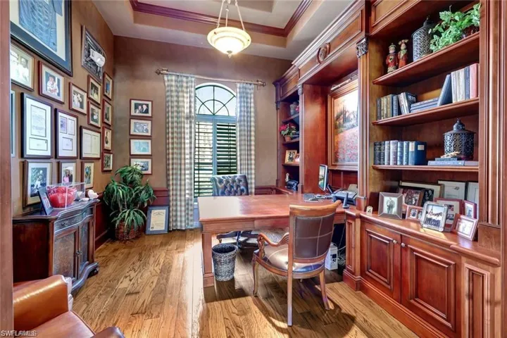 Office area with a raised ceiling, light hardwood / wood-style flooring, and ornamental molding