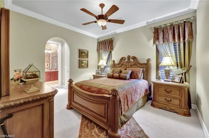 Bedroom with ceiling fan, ornamental molding, light carpet, and connected bathroom