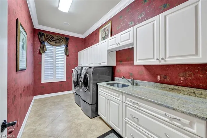 Clothes washing area with cabinets, crown molding, washing machine and dryer, and sink