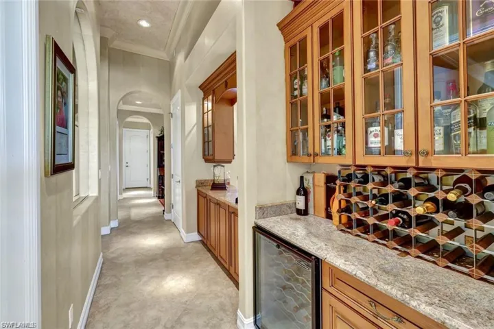 Bar featuring decorative backsplash, light stone counters, beverage cooler, and ornamental molding