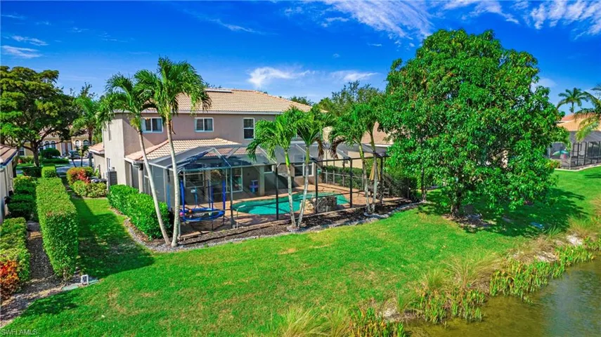 Rear view of property with stucco siding, a tile roof, a yard, a lanai, and a water view