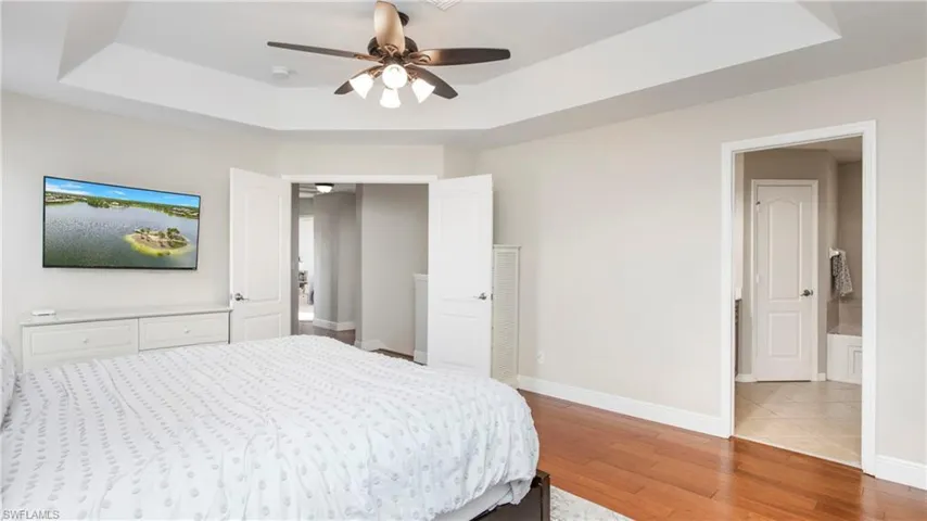 Bedroom with a raised ceiling, wood finished floors, and a ceiling fan