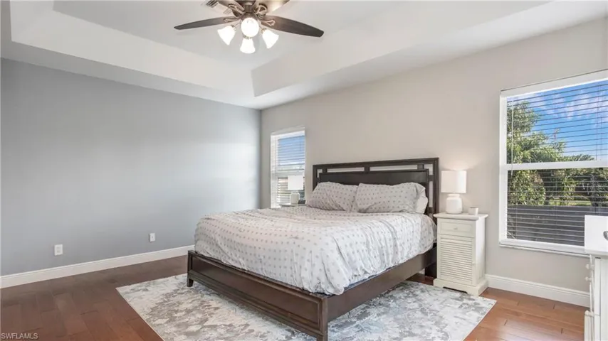 Bedroom with a raised ceiling, hardwood / wood-style flooring, and ceiling fan