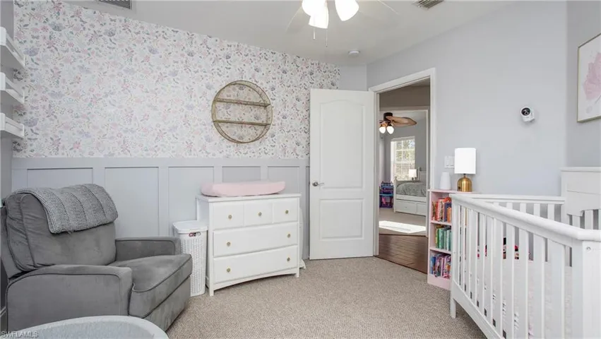 Bedroom with wallpapered walls, a wainscoted wall, a nursery area, light colored carpet, and a decorative wall