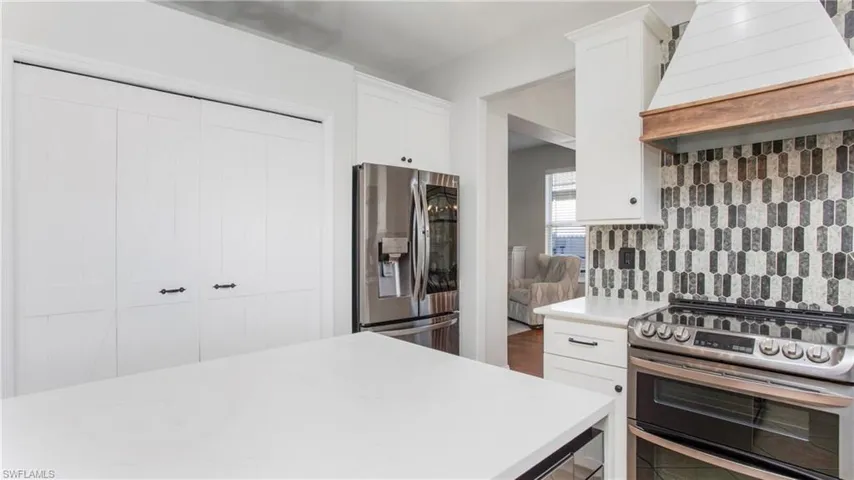Kitchen featuring stainless steel appliances, premium range hood, light countertops, tasteful backsplash, and white cabinetry