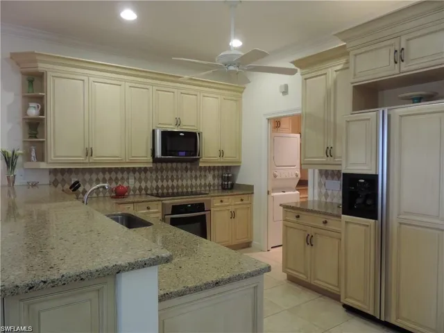 Kitchen featuring stainless steel appliances, backsplash, ceiling fan, and stacked washer / drying machine