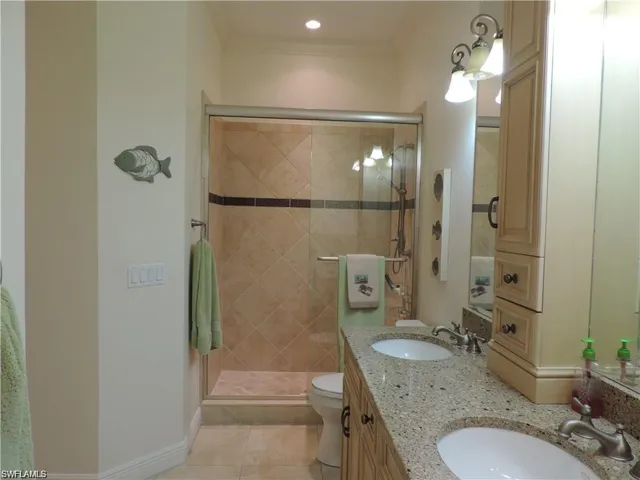 Bathroom with tile flooring, dual vanity, an enclosed shower, ornamental molding, and toilet