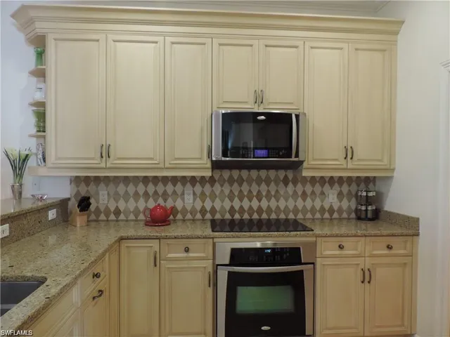 Kitchen with appliances with stainless steel finishes, cream cabinets, tasteful backsplash, and light stone counters