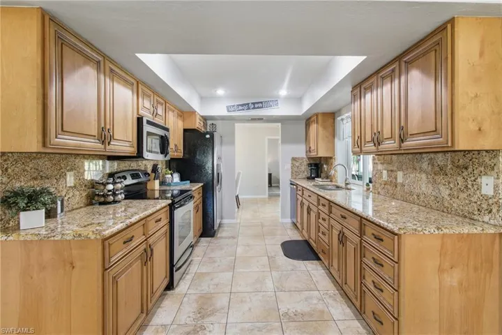 Kitchen with backsplash, a tray ceiling, appliances with stainless steel finishes, and light stone counters