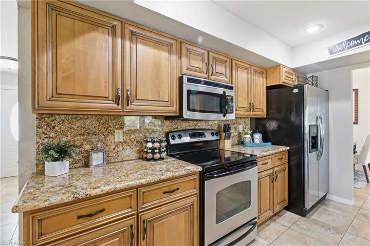 Kitchen featuring stainless steel appliances, light tile patterned floors, brown cabinetry, backsplash, and light stone counters