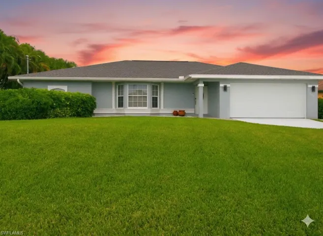 Single story home featuring a front lawn, a shingled roof, stucco siding, driveway, and a garage