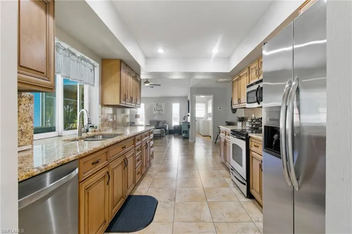 Kitchen featuring stainless steel appliances, light stone countertops, light tile patterned floors, backsplash, and ceiling fan