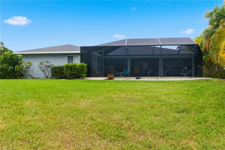 Rear view of house featuring glass enclosure, a lawn, stucco siding, and a sunroom