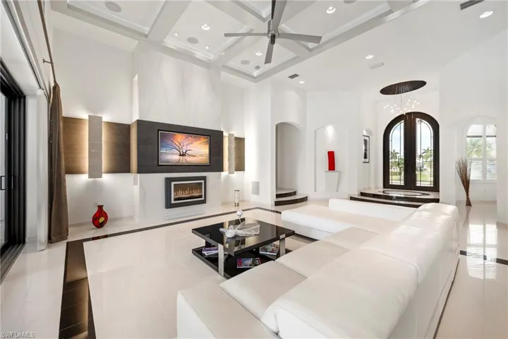 Living area featuring a premium fireplace, coffered ceiling, ceiling fan, arched walkways, and inlaid floor details