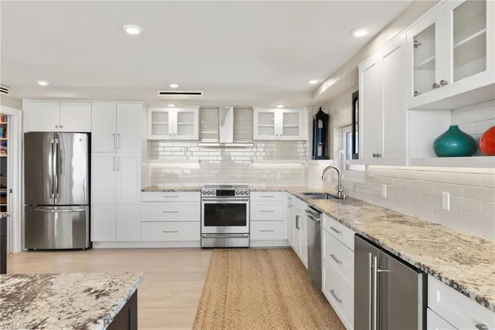 Kitchen featuring stainless steel appliances, a sink, wall chimney exhaust hood, decorative backsplash, and recessed lighting
