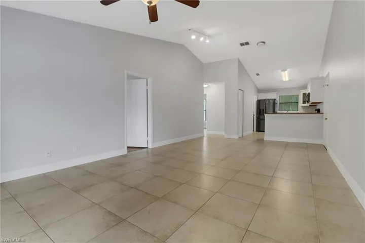 Unfurnished living room featuring rail lighting, ceiling fan, vaulted ceiling, and light tile patterned floors