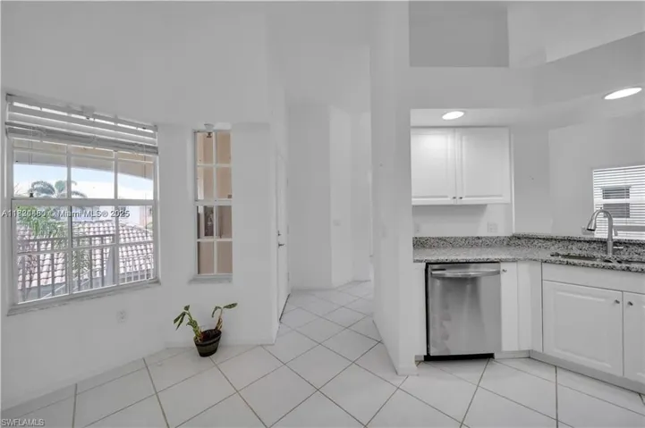 Kitchen with light stone counters, white cabinets, stainless steel dishwasher, and light tile patterned floors