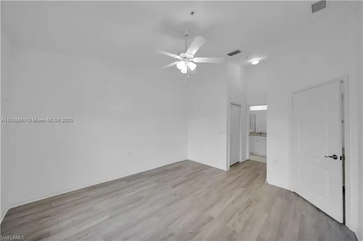 Unfurnished bedroom featuring light wood-type flooring, ensuite bath, a ceiling fan, and a high ceiling