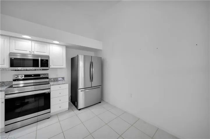 Kitchen with stainless steel appliances, white cabinetry, light stone countertops, and light tile patterned flooring