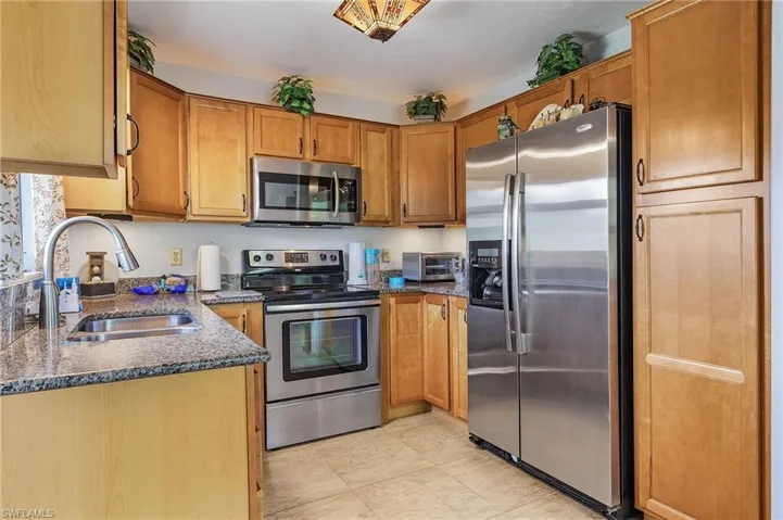 Kitchen featuring light tile patterned flooring, sink, dark stone counters, and stainless steel appliances