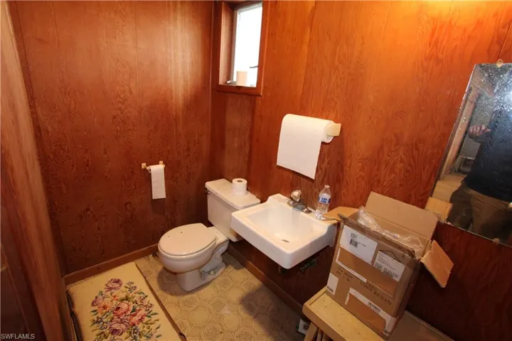 Bathroom with sink, tile flooring, wooden walls, and toilet