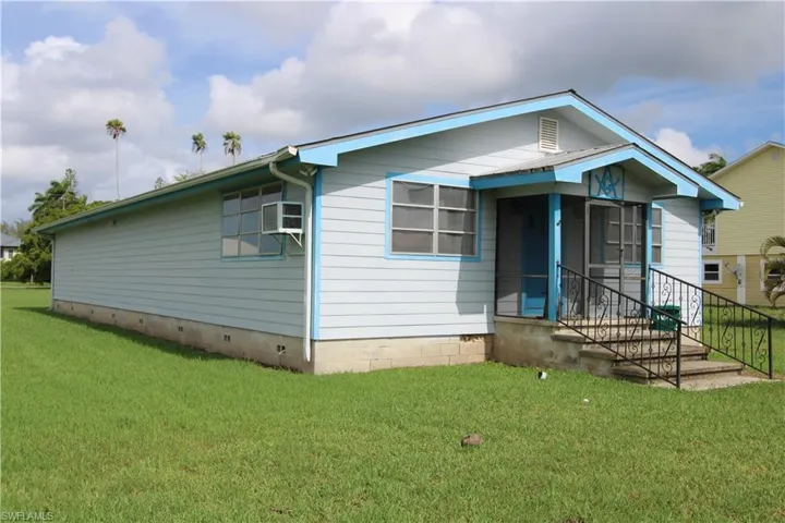 View of front of home featuring a wall mounted AC and a front lawn