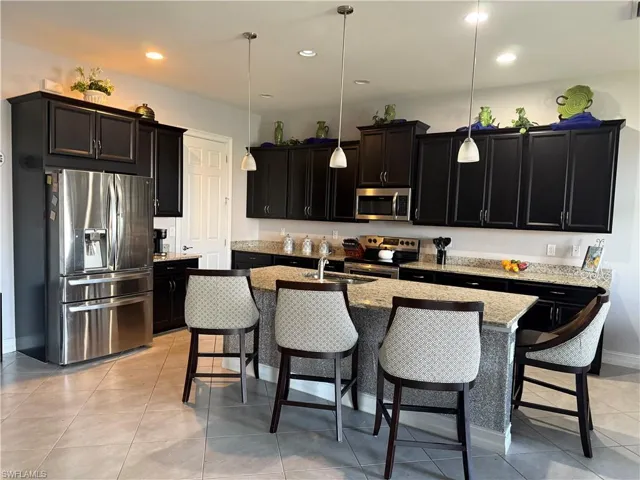 Kitchen with stainless steel appliances, a kitchen bar, dark cabinets, pendant lighting, and recessed lighting