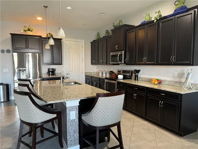 Kitchen featuring light stone counters, appliances with stainless steel finishes, decorative light fixtures, light tile patterned floors, and a breakfast bar
