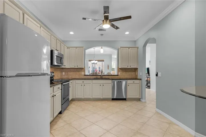 Kitchen with sink, backsplash, cream cabinets, and appliances with stainless steel finishes