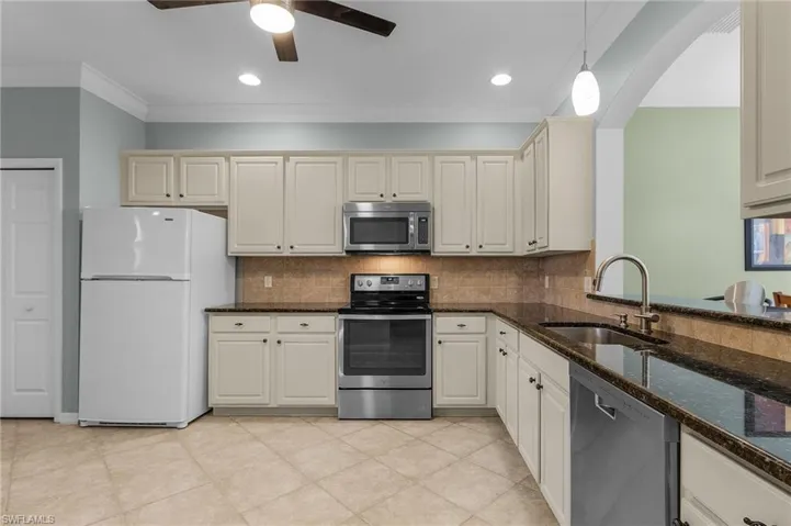 Kitchen featuring sink, dark stone countertops, ornamental molding, pendant lighting, and stainless steel appliances