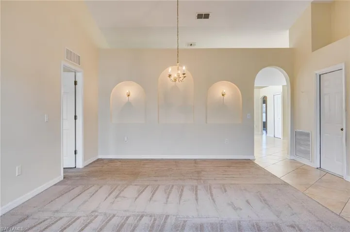 Unfurnished dining area featuring hanging lights, arched walkways, lofted ceiling, light colored carpet, and light tile patterned floors