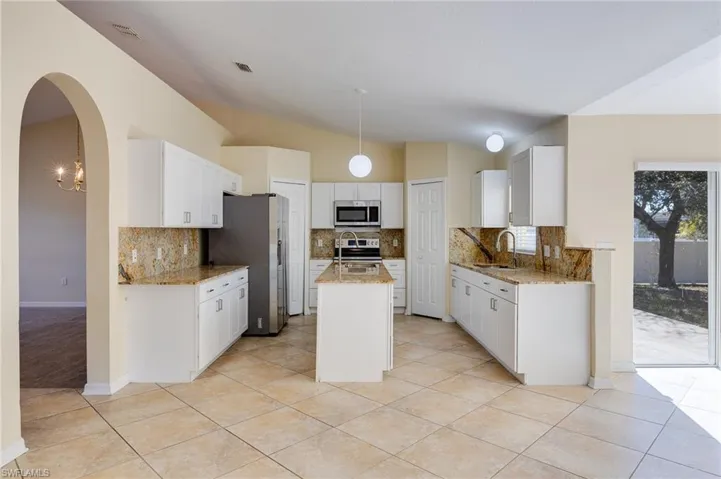 Kitchen with an island with sink, decorative light fixtures, white cabinetry, arched walkways, and backsplash