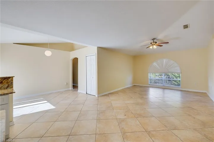 Unfurnished room with arched walkways, a ceiling fan, lofted ceiling, and light tile patterned flooring