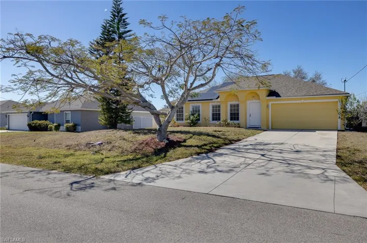 Ranch-style house featuring an attached garage, driveway, solar panels, stucco siding, and a front lawn