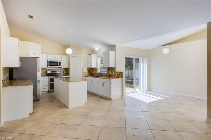 Kitchen with pendant lighting, vaulted ceiling, tasteful backsplash, a kitchen island with sink, and white cabinetry