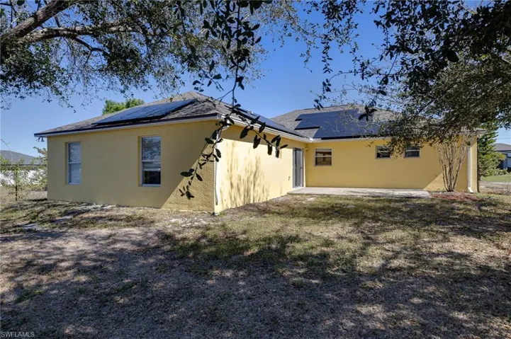 Back of house with a patio area, roof mounted solar panels, stucco siding, a shingled roof, and a yard