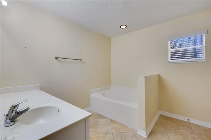 Full bathroom featuring a bath, vanity, a textured ceiling, recessed lighting, and light tile patterned floors