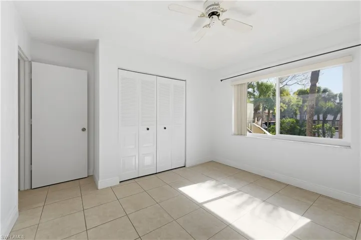 Bright room featuring a large window, tiled flooring, louvered bi-fold closet doors, a solid interior door, and a ceiling fan