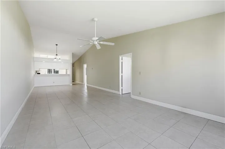 Spacious living area featuring light-toned tile flooring, vaulted ceilings, and a ceiling fan