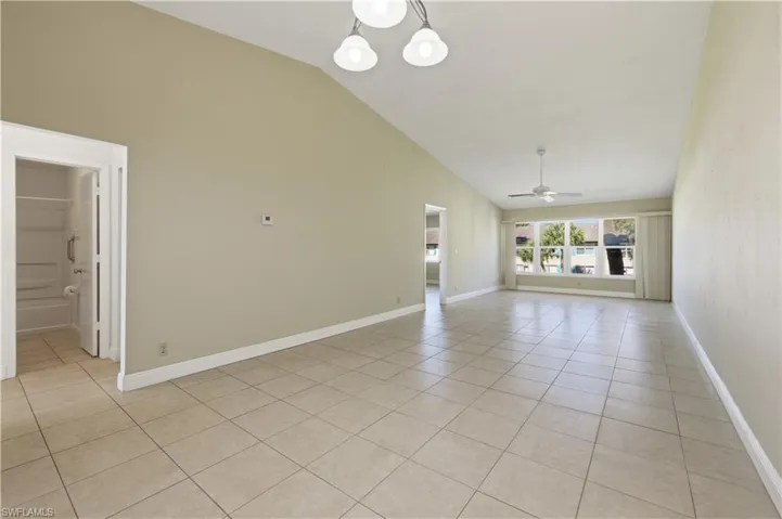 Spacious living area featuring tiled flooring, a vaulted ceiling, a ceiling fan, and large windows with natural light