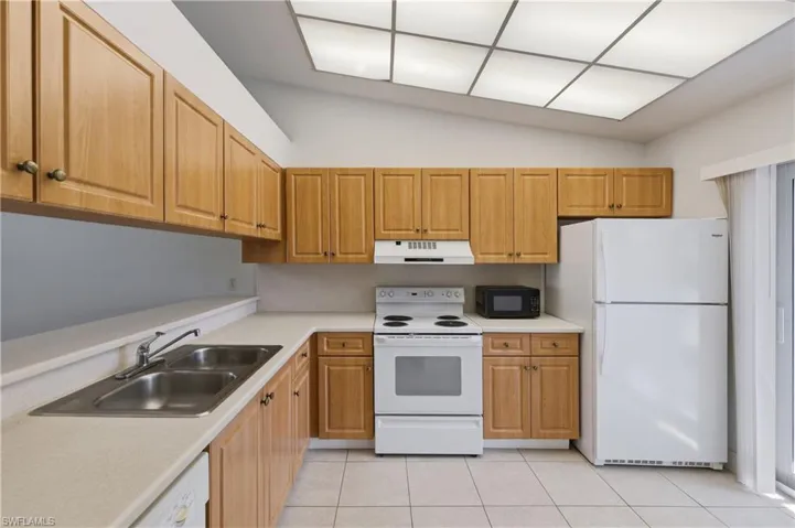 Kitchen featuring wood cabinetry, light-toned countertops, a double stainless steel sink, tile flooring, and an angled ceiling with grid panel lighting