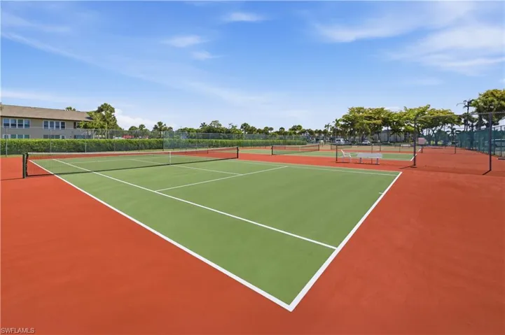 Multiple tennis courts featuring green and orange surfacing, surrounded by fencing