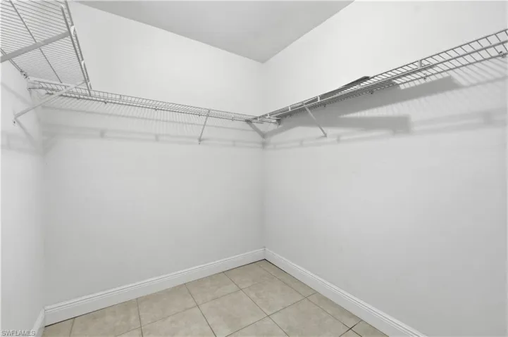 Spacious closet featuring white wire shelving, extending along two walls, with light-toned tiled flooring and white baseboards