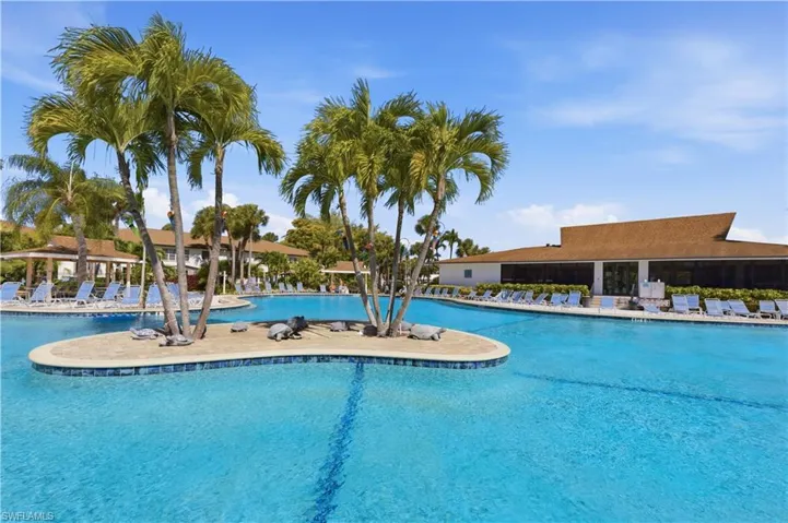 Expansive outdoor pool area featuring a large swimming pool with decorative tile accents, an integrated island with palm trees, and multiple lounge chairs for relaxation