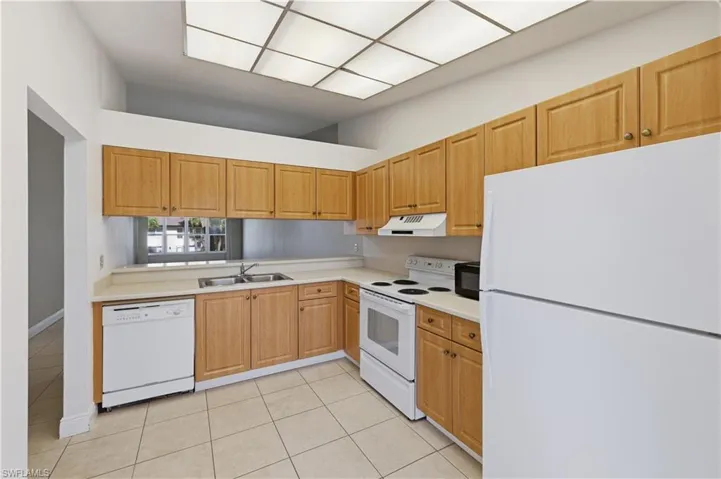 Kitchen featuring light wood cabinetry, light countertops, white appliances, and tiled flooring