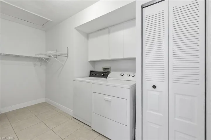 Dedicated laundry area featuring tile flooring, white cabinetry, louvered bi-fold doors, and built-in shelving with an integrated drying rack