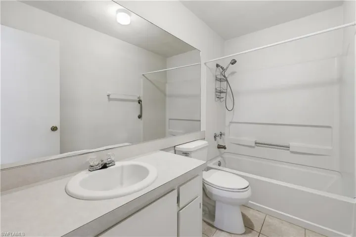 Bathroom featuring a full vanity with an integrated sink, a large wall-mounted mirror, a toilet, a full bathtub with an overhead shower, and tiled flooring