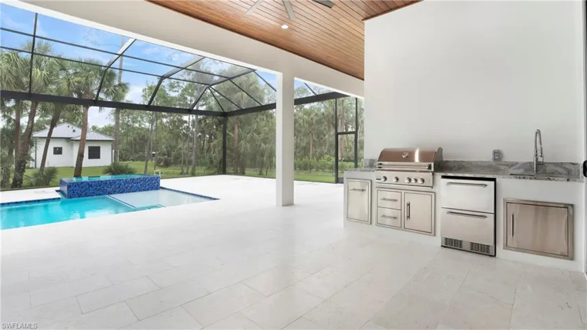 Outdoor pool featuring a patio area, an outdoor kitchen, a sunroom, and glass enclosure