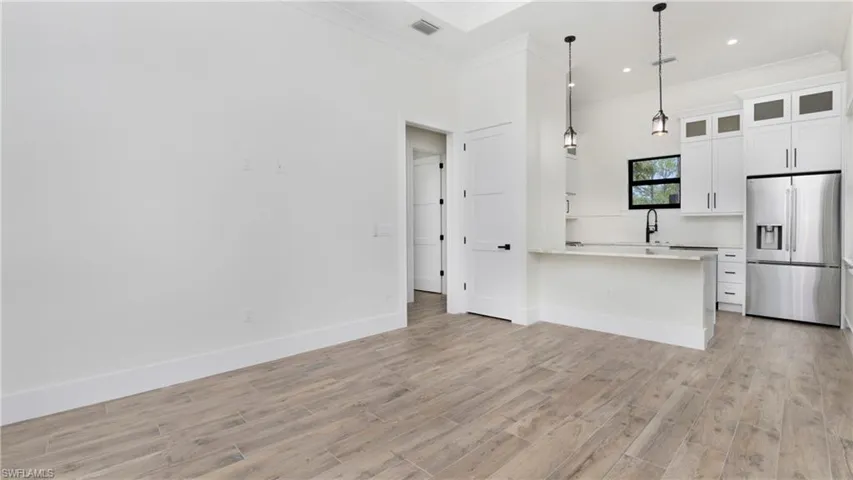 Kitchen with stainless steel refrigerator with ice dispenser, decorative light fixtures, white cabinetry, a peninsula, and glass insert cabinets